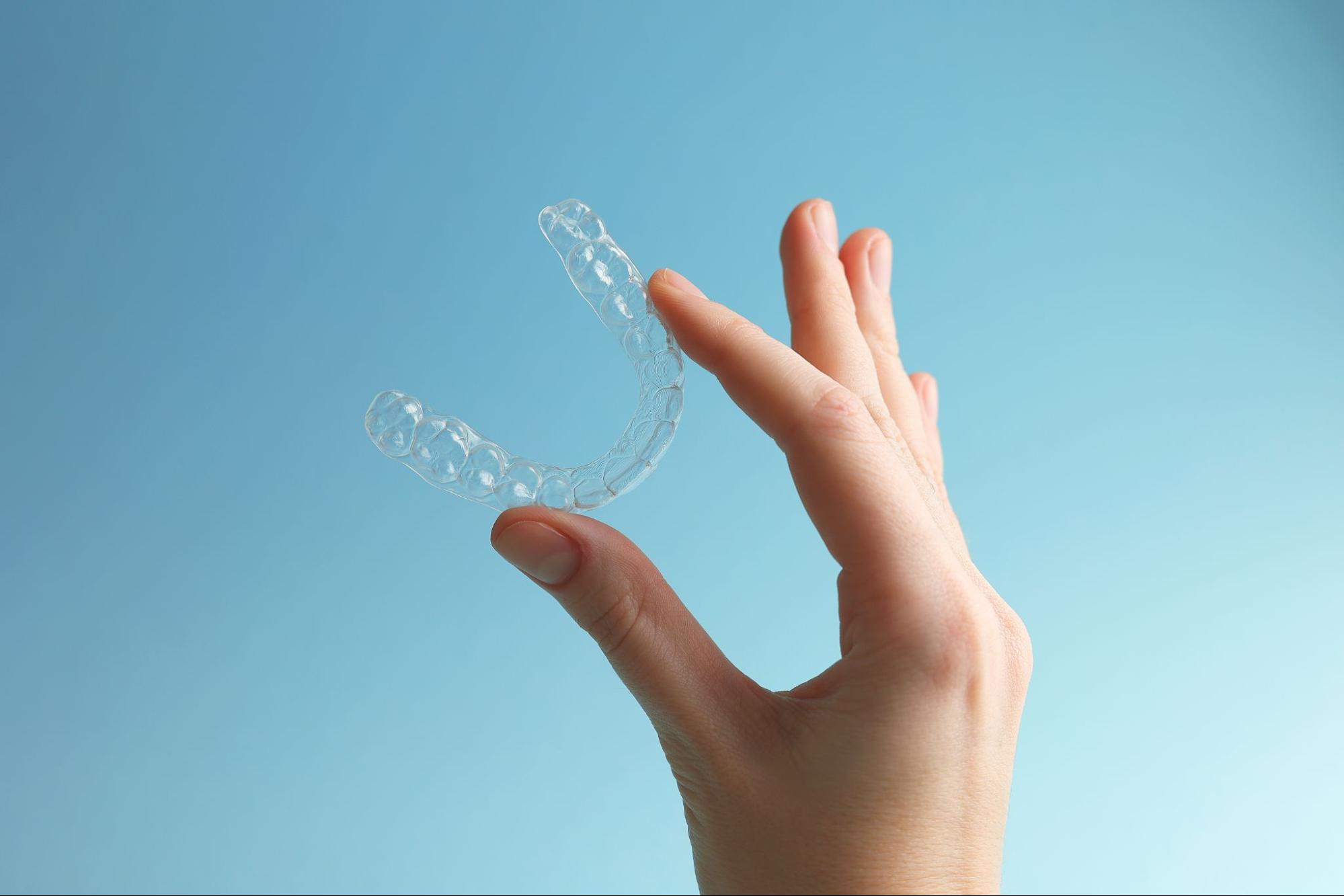 Image d’une main tenant un aligneur transparent dans les airs