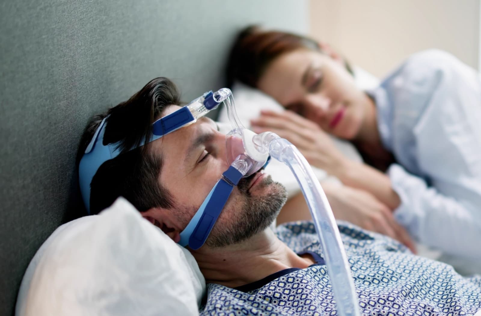 man sleeping next to partner, wearing sleep apnea mask