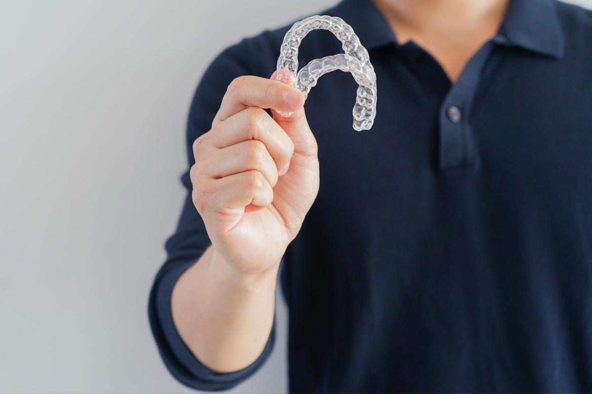 Personne en chemise bleu marine tenant des gouttières d'alignement orthodontique transparentes vers la caméra.