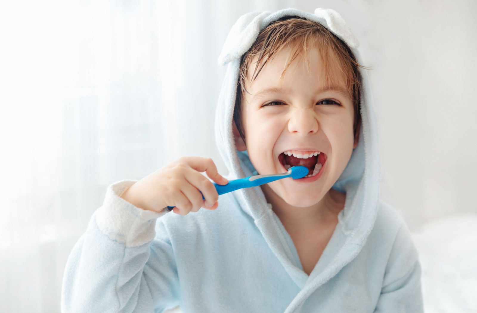 Image d'un jeune enfant souriant, se brossant les dents avec une brosse bleue